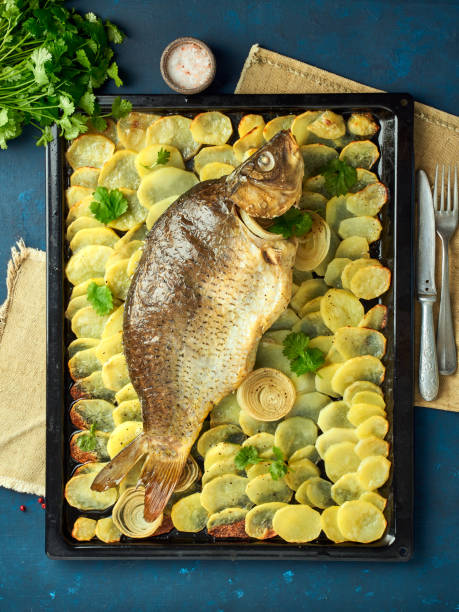 Baked carp, whole fish from the oven with sliced potatoes on a large tray. Traditional polish dish