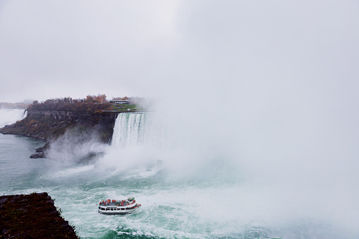 On a overcast day tourist enjoying Niagara falls excursion boat ride. This is one of the most visited attractions at the borders of US and Canada. Visitors enjoy the thundering misting thrill which lasts for about 15-20 minute boat ride in the very heart of Niagara falls.