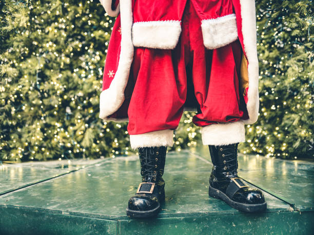 Santa Clause posing in front of large Christmas tree in big North American city. Red suit, boots and all. Ready for Christmas.