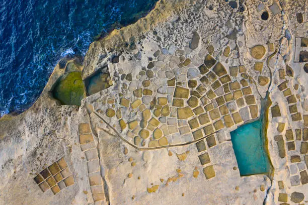 Aerial view of salt pans on Gozo island. Blue sea, rocks, waves. Malta island