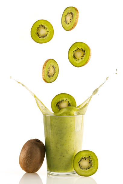 Delicious and nutritious slices of kiwi fall into a glass of fresh kiwi smoothie on white background stock photo