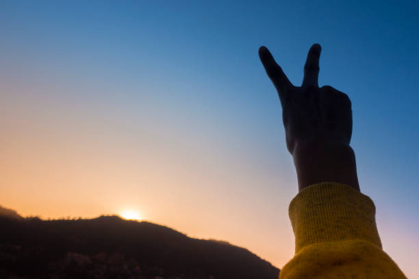 istock Cropped hand gesturing Peace sign against the sun during sunset. 1195638946