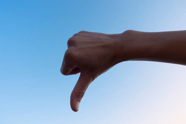 istock Cropped hand gesturing thumb down, sign against the clear sky. 1195639031