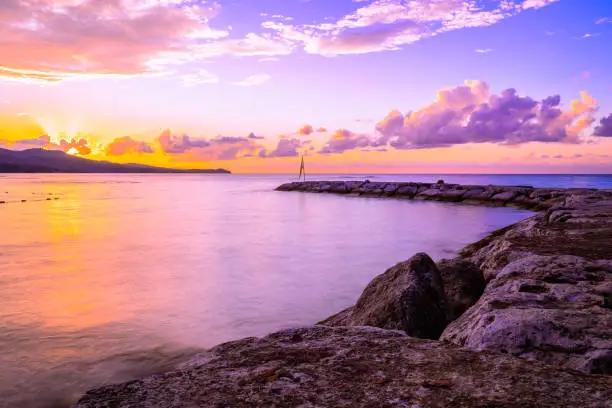 Magnificent sunset with colorful sky colors as sun sets behind mountains on tropical Caribbean island landscape. Beautiful end to perfect romantic summer evening. Calm beach ocean waters on coastline.