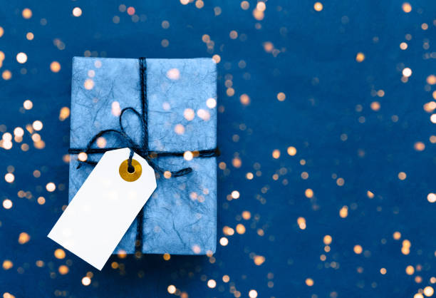 Blue gift box with gift tag on blue background. Holiday background. Copy space for text, top view. Color of the year 2020 classic blue toned.