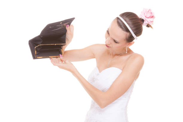 Bride with empty wallet. Young girl holding purse looking for money cash. Wedding expenses costs, expenditure. Finance concept. Woman in white wedding dress isolated on white background.