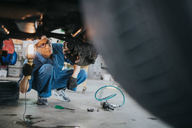Thai mechanic man with lamp working at car auto repair shop stock photo ian car mechanic with lamp working at auto repair shop, Bangkok Thailand,copy space mechanic working under car stock pictures, royalty-free photos & images
