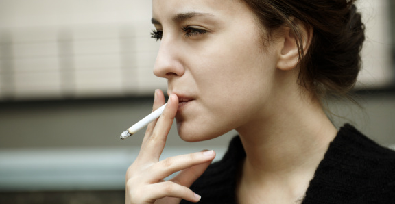 Profile view of a young redhead woman smoking a cigarette in nature. Copy space.