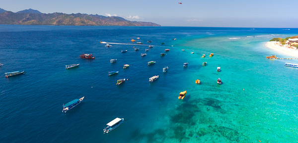 tropical island with white sandy beach and blue transparent water and coral reefs. Aerial shooting, speedboats, longtail boats, Gili Trawangan island Indonesia