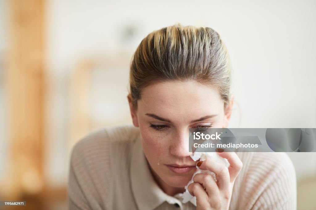 Grief-stricken young woman looking down and wiping tears with napkin at therapy session, emotions concept Grief-stricken woman wiping tears Women Stock Photo