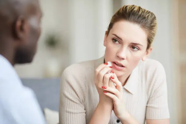 Photo of Puzzled girl listening to psychologists advice and wiping tears at therapy session