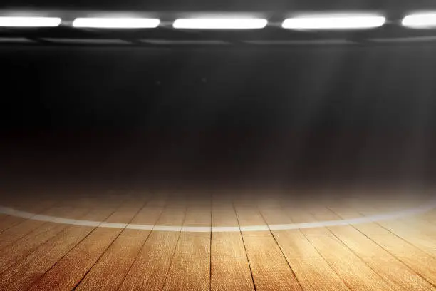 Close up view of a basketball court with wooden floor and spotlights over dark background