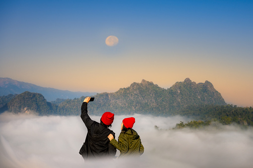 couple lover are enjoy the nature life of travel on the peak of mountain with full around of the nature mist on the hills