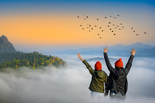 couple lover are enjoy the nature life of travel on the peak of mountain with full around of the nature mist on the hills, cheerfully life of the nature surrounding