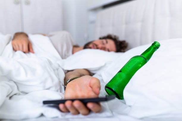 sms mentre si è ubriachi. giovane sdraiato a letto ubriaco mortale che tiene una bottiglia vuota di alcol. intossicato dall'alcol. alcolismo ubriachezza abituale concetto di abitudine perniciosa - exhaustion tired men after work foto e immagini stock