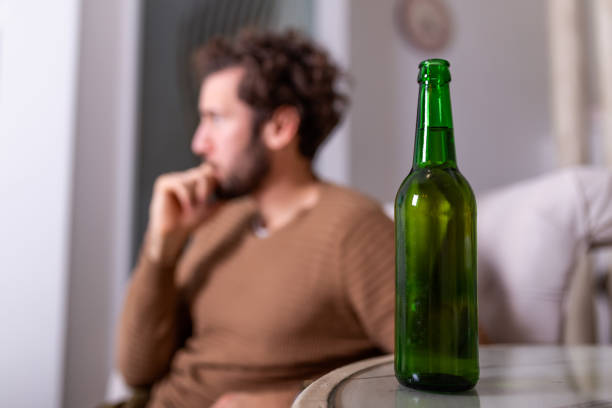 アルコールのボトルの後ろで飲んでいる匿名のアルコール人のシルエット。アルコール習慣と戦う男、自宅でソファに座って飲む - eastern european caucasian one person alcoholism ストックフォトと画像