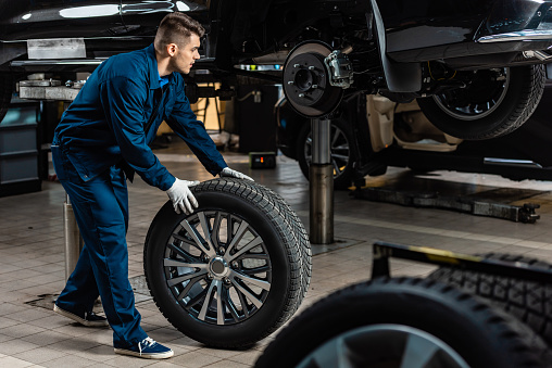 joven mecánico sosteniendo la rueda del coche cerca del coche levantado en el taller photo