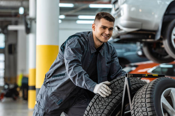 istock handsome, smiling mechanic holding new tire in workshop 1195719258