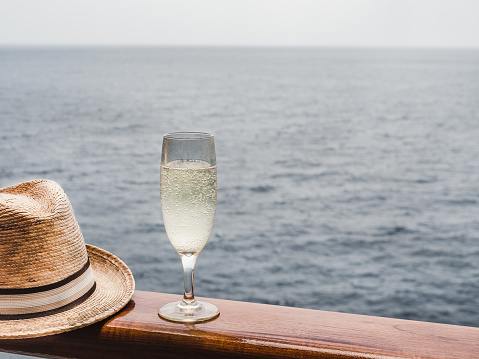 Beautiful champagne glass on the open deck of a cruise liner against the backdrop of blue sea waves. Side view, close-up. Concept of leisure and travel
