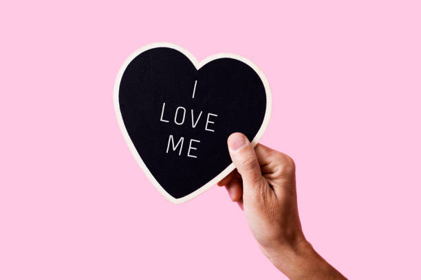 text I love me in a heart-shaped sign closeup of a man holding a black heart-shaped sign with the text I love me written in it, on a pink background vanity stock pictures, royalty-free photos & images