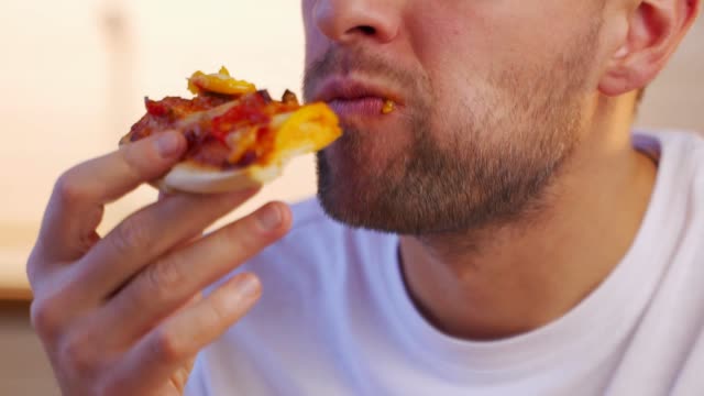 Portrait of a young beautiful man eating a slice of pizza