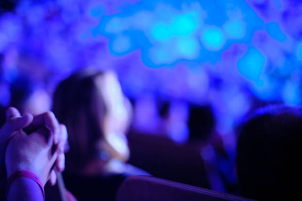 istock Unrecognizable blurry audience of a modern theatre event, illuminated by blue stage light 1195728522