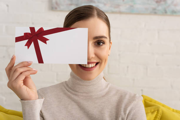 schöne mädchen abdeckung gesicht mit geschenk-karte vorlage und lächelnd in der kamera - geschenkkarte fotos stock-fotos und bilder