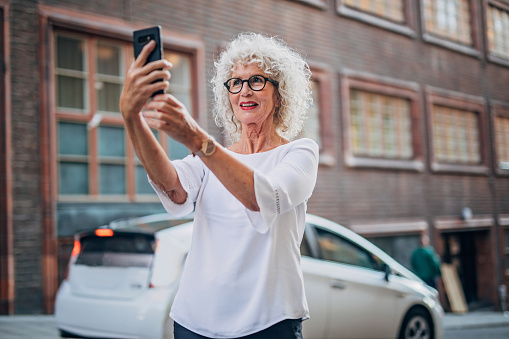 One woman, modern mature lady with gray hair, taking a selfie with mobile phone.