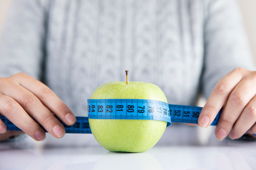 Young woman holding a tape measure on green apple to show eating healthy