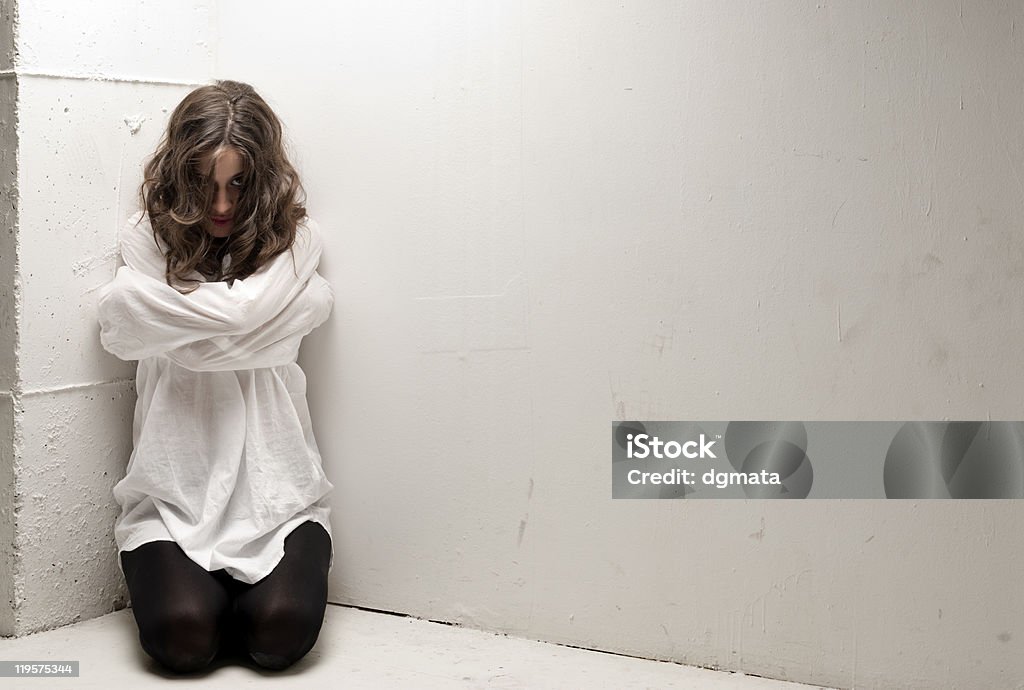An insane woman with straitjacket on knees looking at camera Young insane woman with straitjacket on knees looking at camera. On AdobeRGB.  Straitjacket Stock Photo