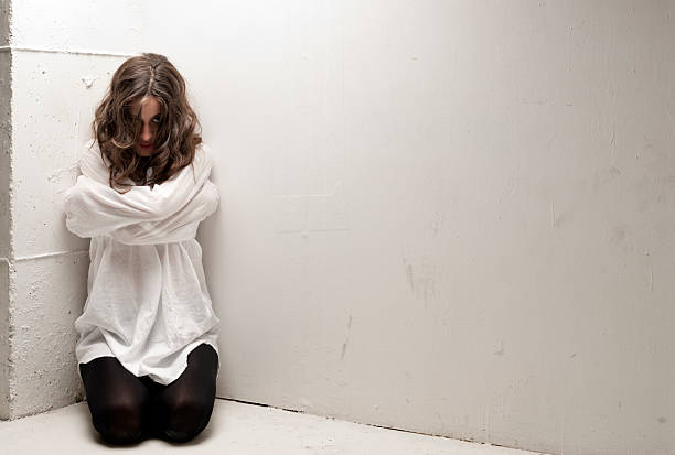 An insane woman with straitjacket on knees looking at camera stock photo