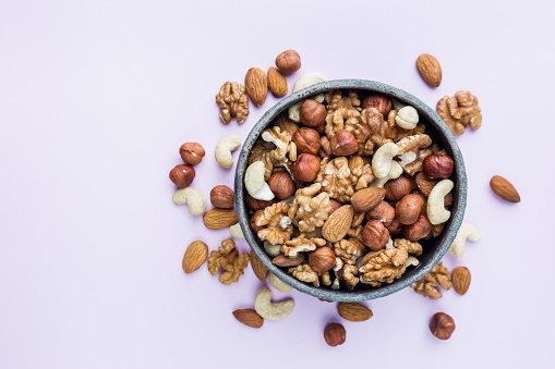 Almond, walnut, hazelnut and cashews flat lay. Nuts in a bowl on pink background, top view