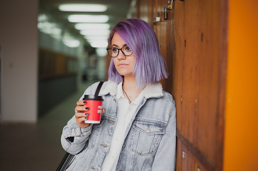 Young attractive women with purple hair in denim jacket standing in the hall and