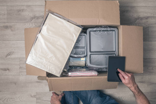 istock man shopper using tablet checking order sitting on floor at home and opening carton box with stationery. parcel from internet shop. Delivery service. Top view. 1195757787