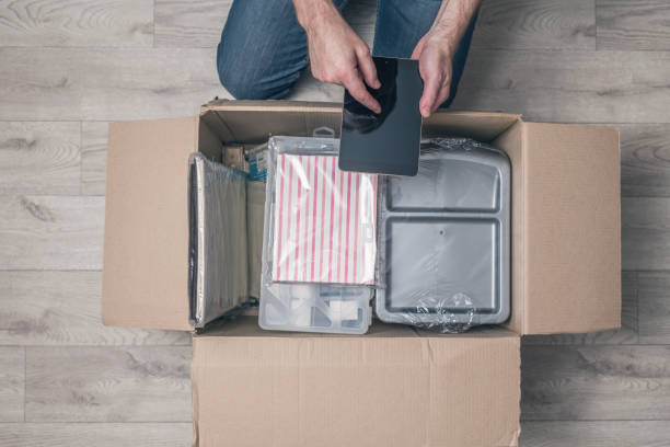 istock man shopper using tablet checking order sitting on floor at home and opening carton box with stationery. parcel from internet shop. Delivery service. Top view. 1195757887