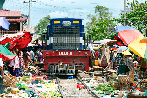 Railway Bazaar, Mandalay, Myanmar. Fruit and vegetable traders sitting with their wares on the active railway line scatter with the arrival of a train, leaving some of their produce between the rails on the track and sleepers until the train has departed at the open air market at Railway Bazaar, Mandalay, Myanmar