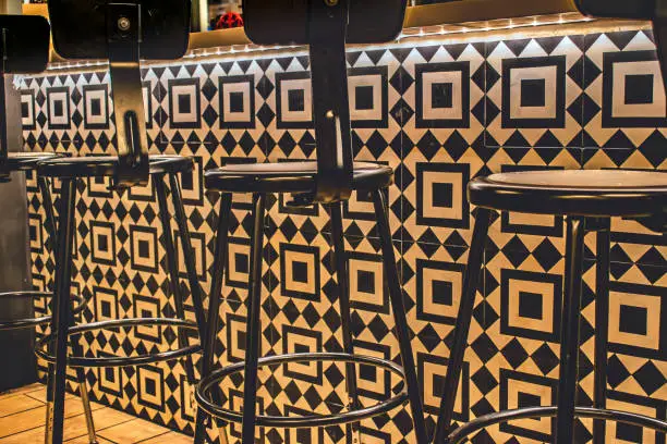 Black bar stools against a black and white mosaic tile wall under the illuminated bar
