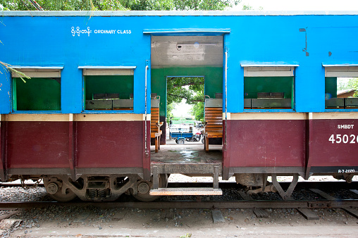 Railway Bazaar, Mandalay, Myanmar. A three-wheeler utility truck seen through the open doors of an ordinary class railway carriage that has emptied on arrival at the bazaar. Fruit and vegetable traders sitting with their wares on the active railway line scatter with the arrival of a train, leaving some of their produce between the rails on the track and sleepers until the train has departed at the open air market at Railway Bazaar, Mandalay, Myanmar