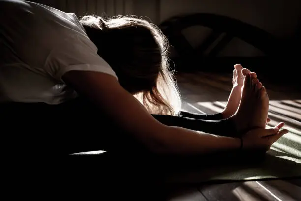 Photo of Young woman stretching in yoga pose on mat, silhouette in dark