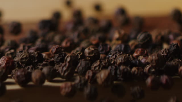 Scattering black pea pepper on kitchen table macro shot