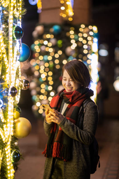 istock Young woman standing by Christmas lights and typing message 1195806208