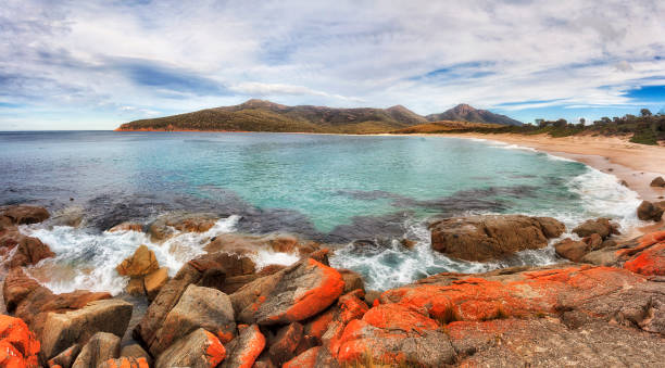 Tas Winegrall beach rocks pan Red eroded boulders around WIneglass bay and white sand beach in Freycinet national park of Tasmania on a sunny day - wide panorama. tidal inlet stock pictures, royalty-free photos & images