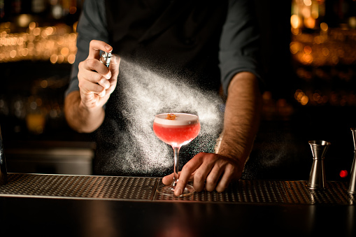 Male bartender sprays small glass with delicious alcohol drink