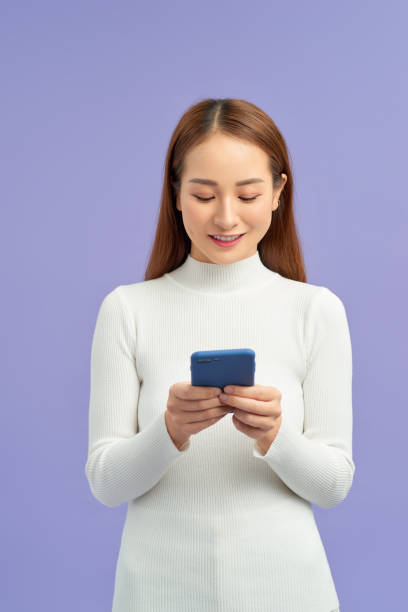 istock attractive asian woman using smart phone isolated on violet background 1195842475