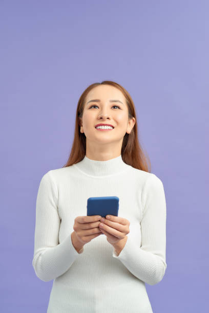 istock attractive asian woman using smart phone isolated on violet background 1195842478
