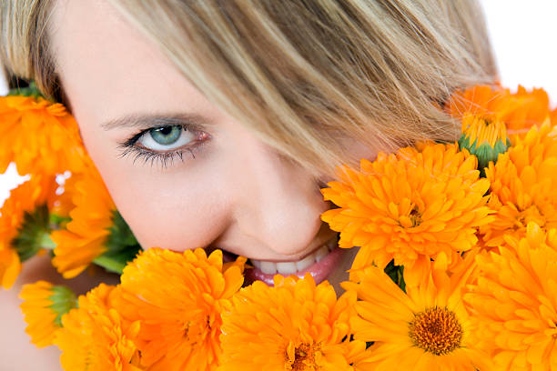 A smiling young woman puling petals off of a large orange flower.