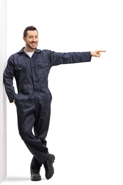 istock Male worker in a uniform leaning on wall and pointing to the side 1195844160