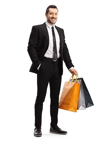 Full length portrait of a man in a black suit holding shopping bags and smiling isolated on white background