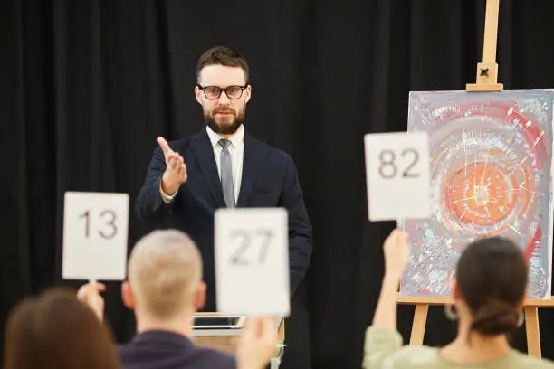 Businessman in suit suggesting lot to the people while they raising their signs during auction