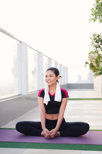 Young beautiful Asian woman sitting on yoga mat and smiling in morning. Sport and healthy lifestyle.